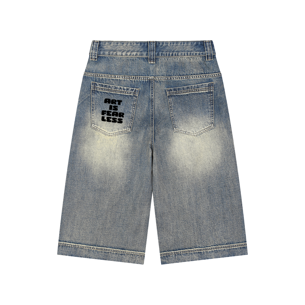 Back view of light-wash denim shorts with a black graphic print on the left back pocket reading 'ART IS FEAR LESS', shown on a plain white background.
