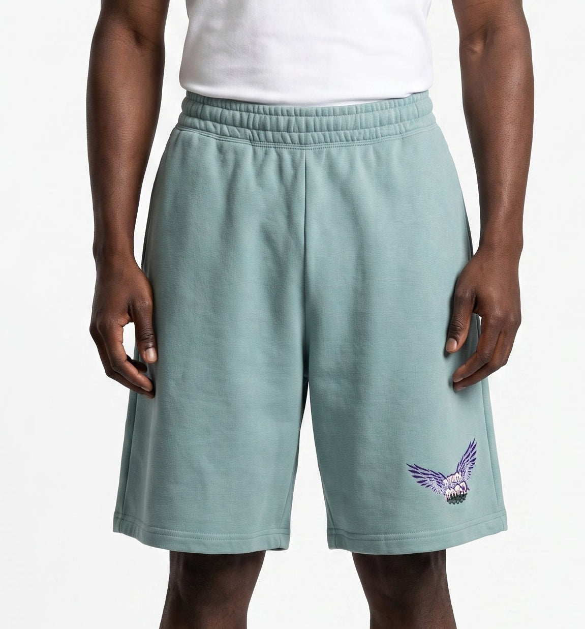 A man modeling a white sleeveless tank top and sage green athletic shorts with a purple and white bird logo on the left leg, set against a plain light gray background.
