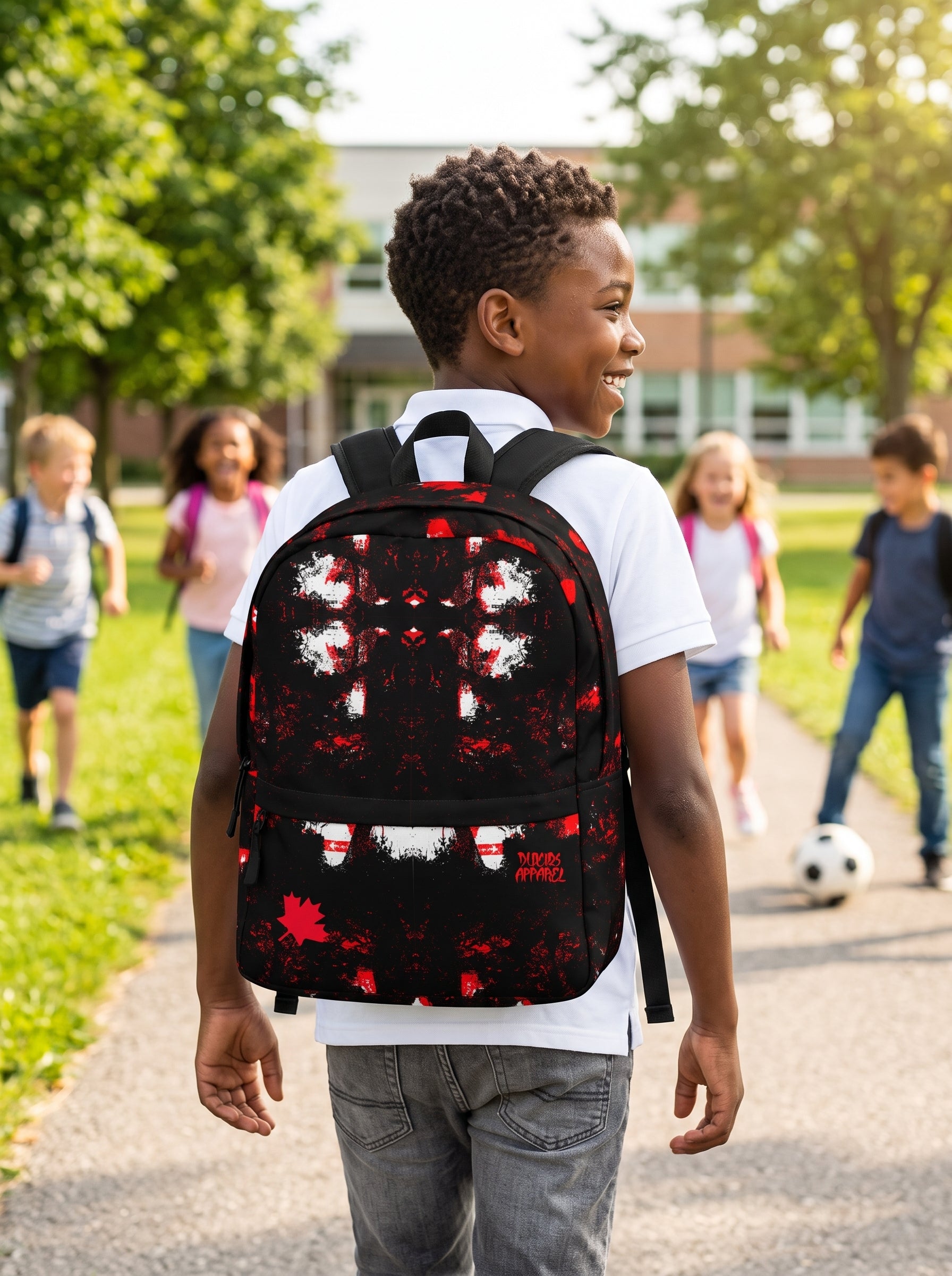A boy walking on a school path wearing a black backpack with a red and white maple leaf pattern, with other children blurred in the background.