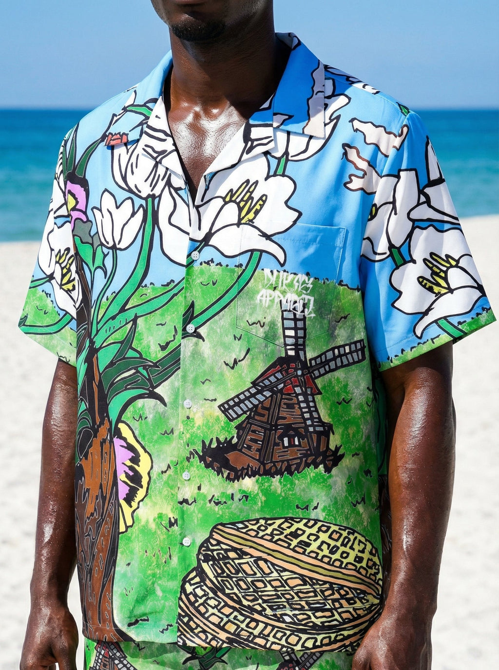 Person wearing a colorful shirt and shorts with a windmill design on a beach.