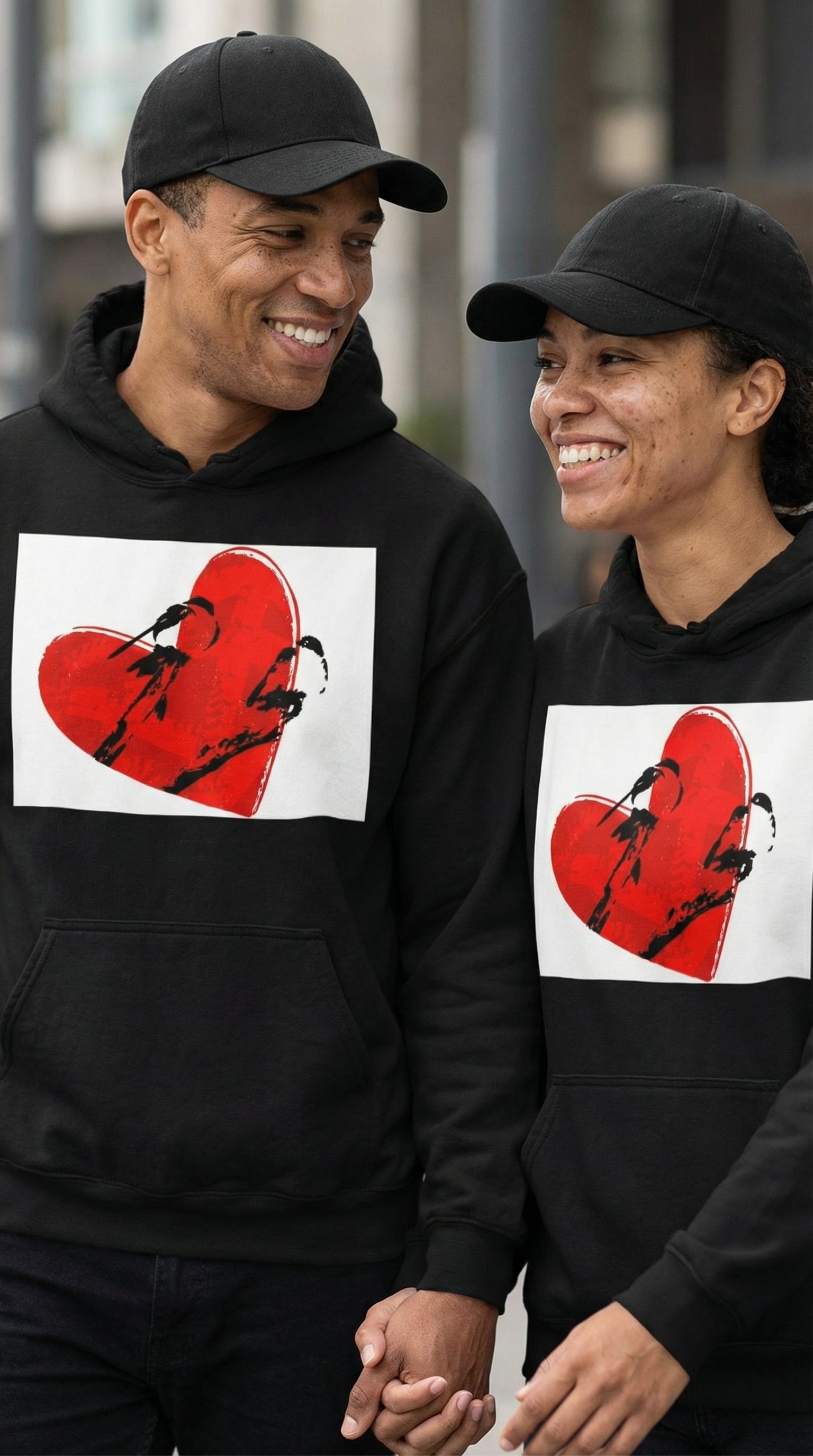 Two people wearing black hoodies with a red heart design on a blurred background